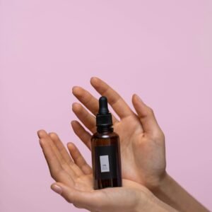 Close-up of a brown dropper bottle held by hands against a pink background, representing natural skincare.