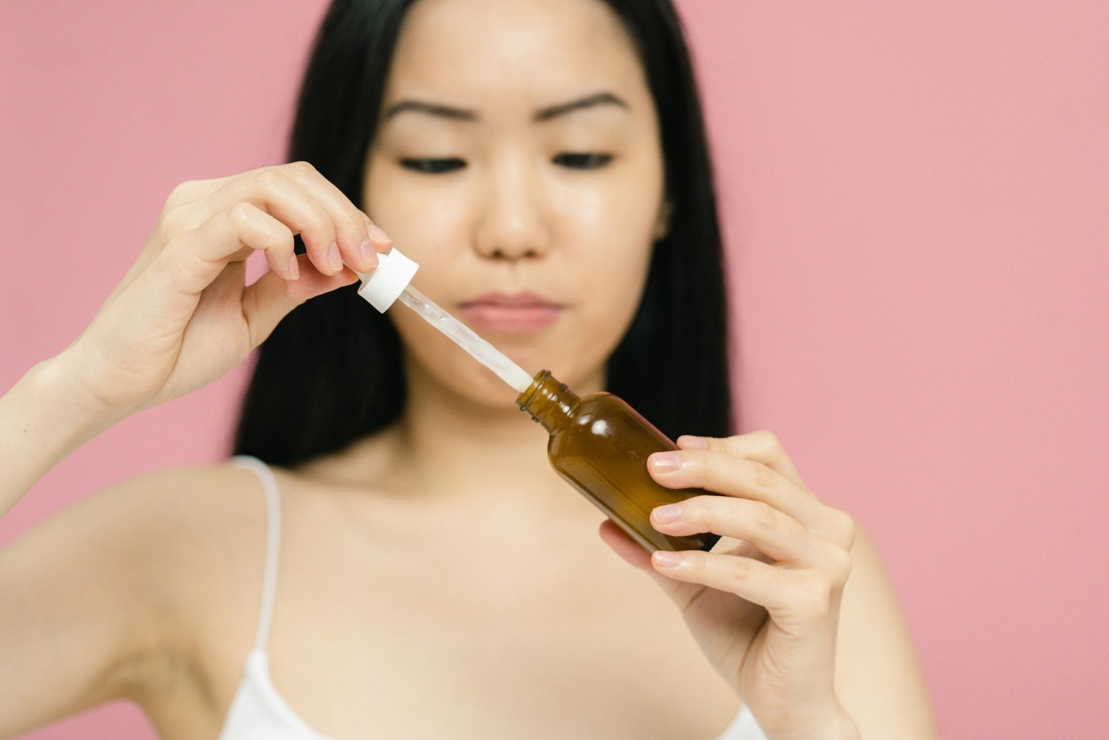 Close-up of a woman holding a serum bottle with a dropper, focusing on skincare.